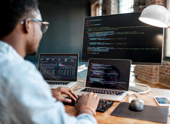 A programmer using two laptops and a display monitor to develop on.